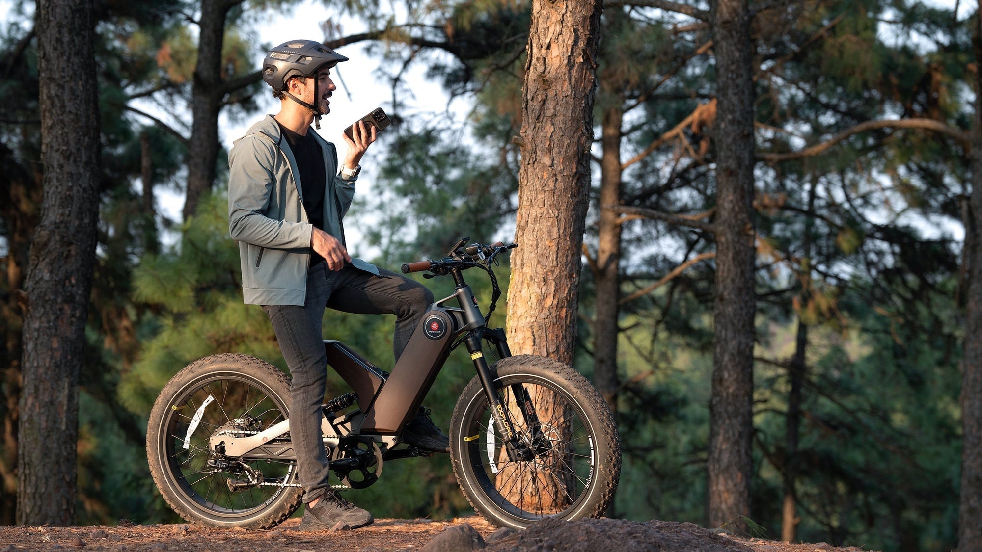 Man in helmet with electric bike, using phone in a forest.