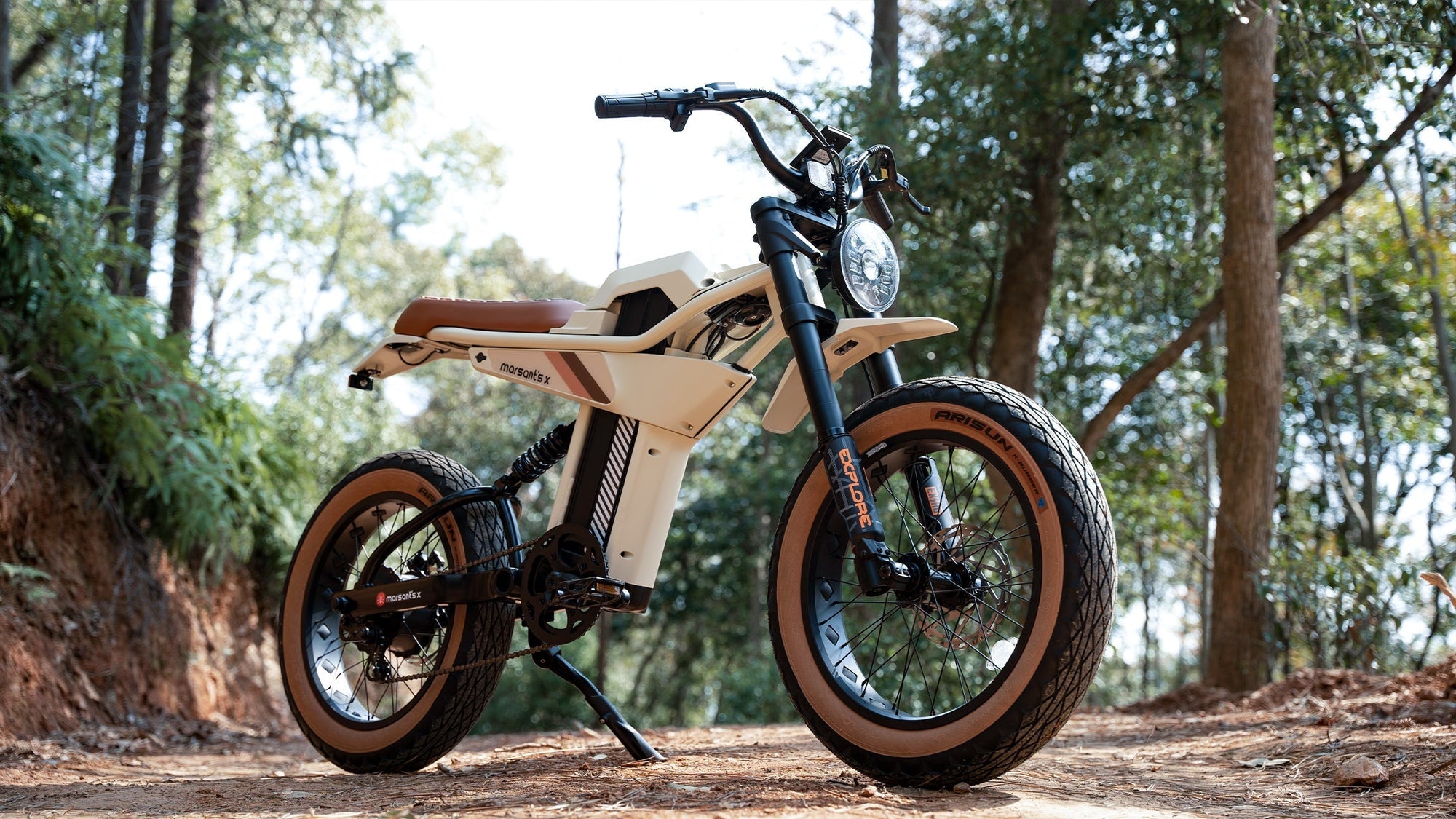 A sleek Marsant's X electric bike with large tires is parked on a dirt path in a lush forest.
