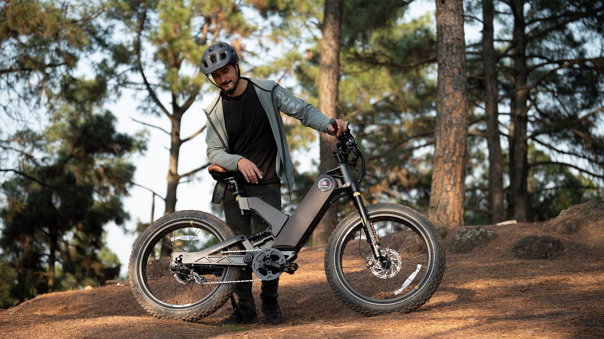 A man in a helmet stands beside his electric bike on a forest trail, ready for an adventure.