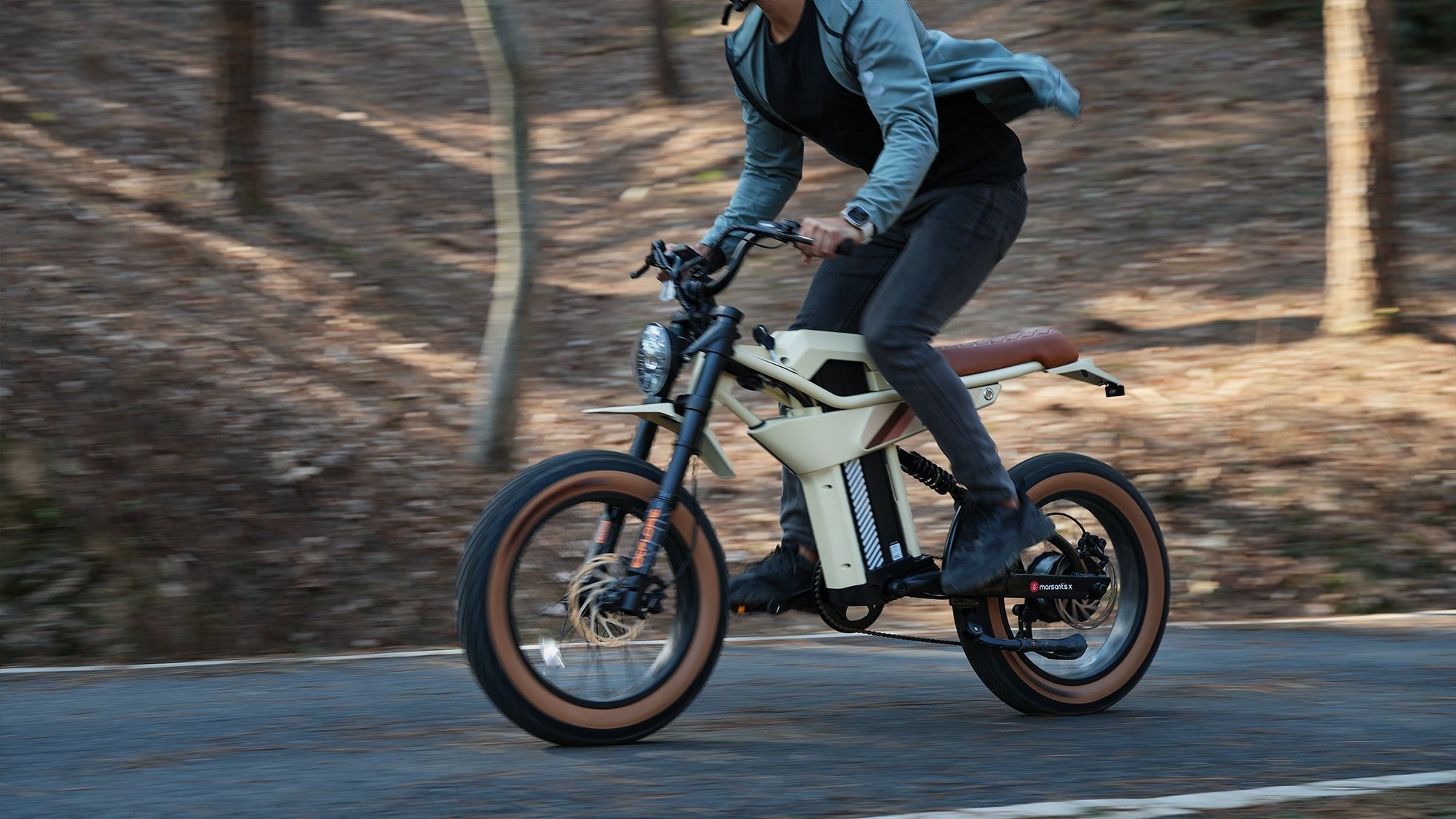 Person riding beige fat tire e-bike outdoors near trees.